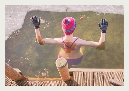 A wild swimming woman wearing a beanie hat, partaking in cold water therapy by dipping in ice water.