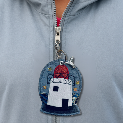 A handmade Burry Port Lighthouse Ocean Charm made from denim and glitter felt, with a sparkling red top and a silver whale-tail charm attached.