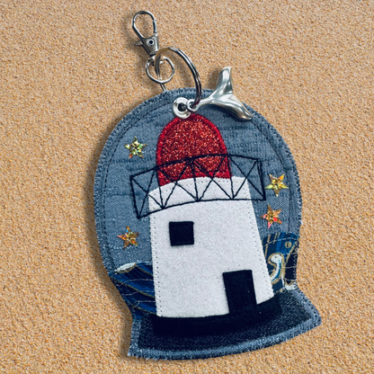 Close-up of the Waves & Wild Water Burry Port Lighthouse keyring charm, showing its glitter dome, denim base, and silver whale-tail detail.