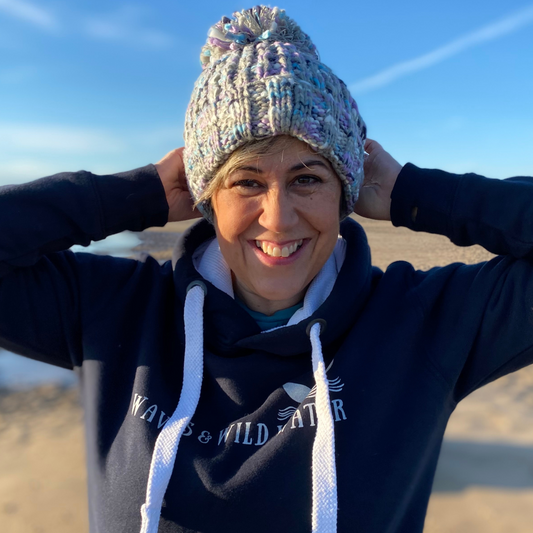A woman on the beach wearing a chunky knitted beanie hat with a pom pom.