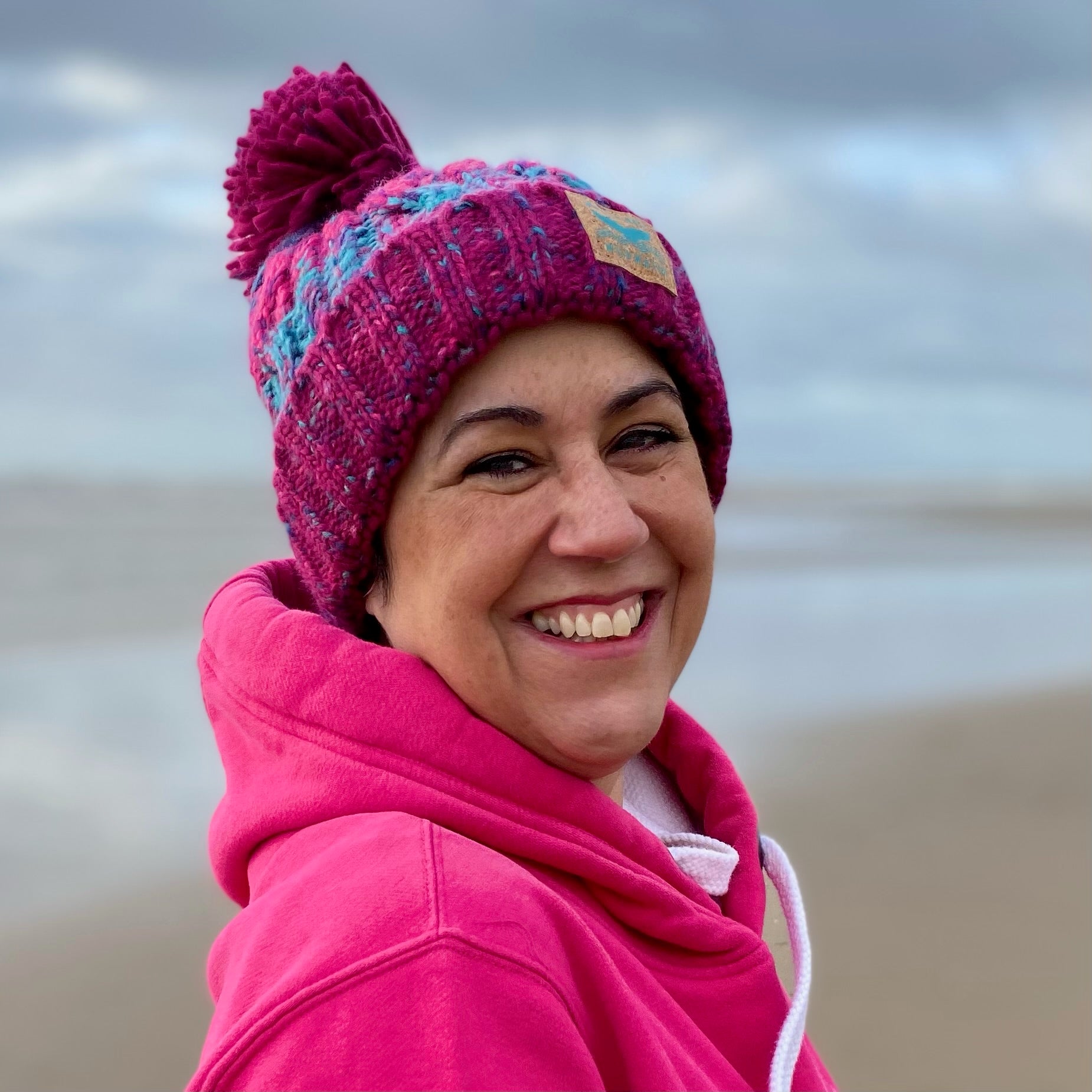 Woman wearing a pink knitted beanie hat with a pom pom.