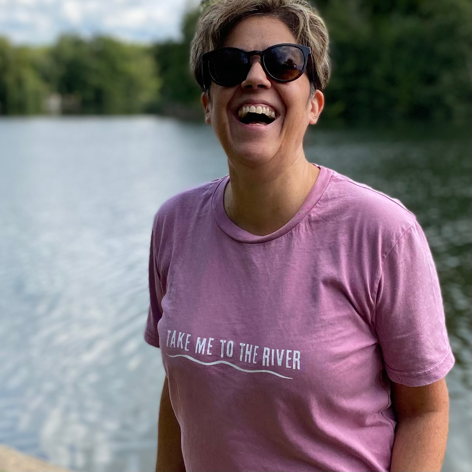 A woman laughing and wearing a pink t-shirt with 'Take me to the river' printed on the front.