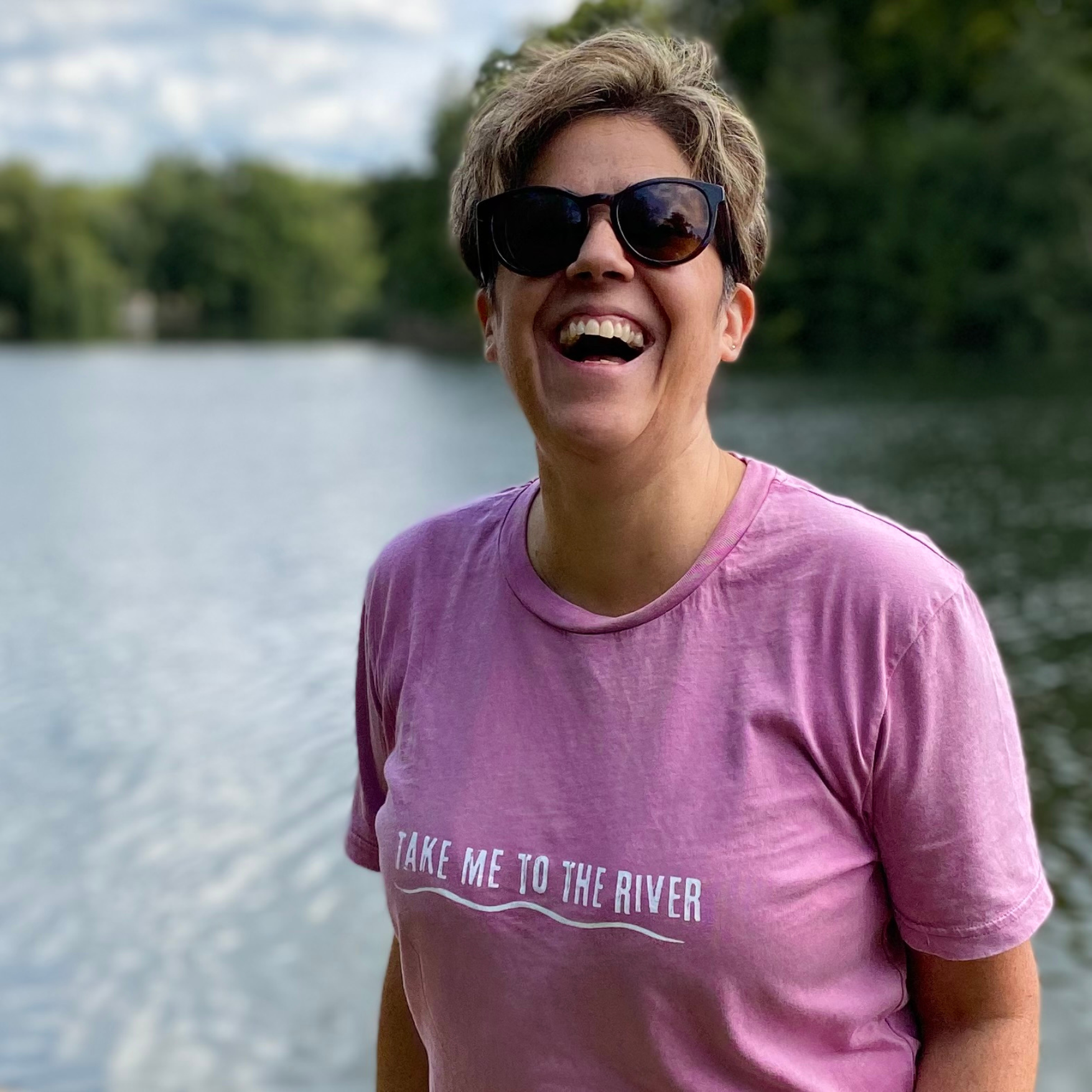 Woman stood by a river and wearing a pink t-shirt and sunglasses