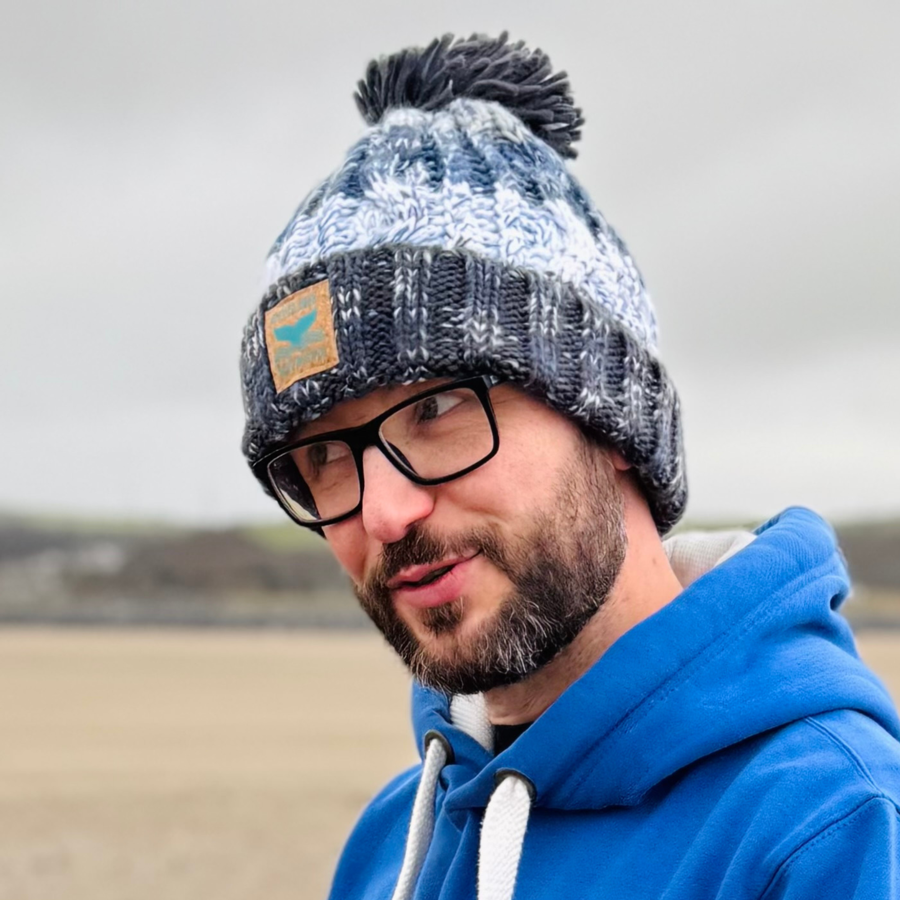 This fab knitted beanie hat is shown in shades of grey with a great big fat pom pom on the top!