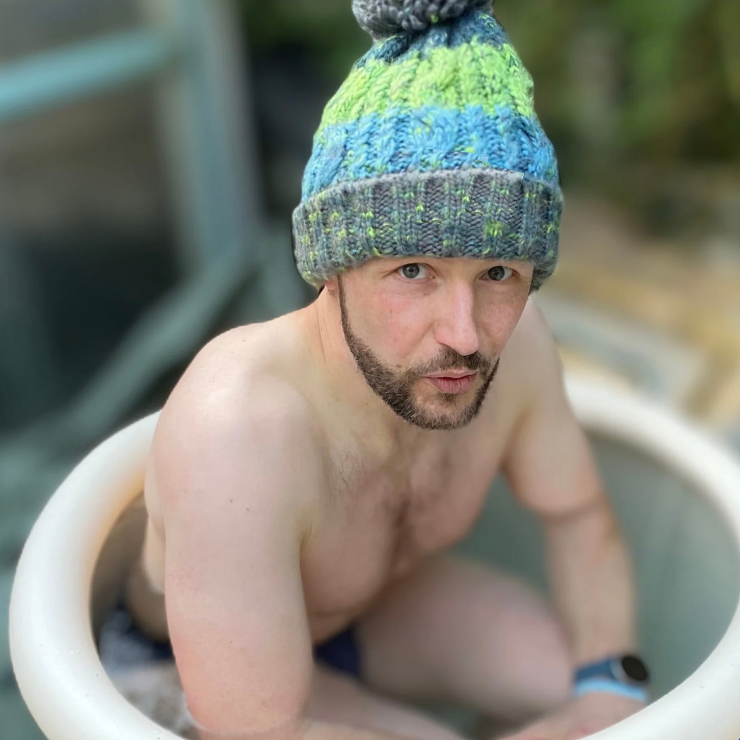 Waves and Wild Water owner, Glenn, works on his cold tolerance in an ice tub. Following advice from cold water therapist Claire, he stops the heat leaving through his head by wearing his River bed knitted beanie hat.