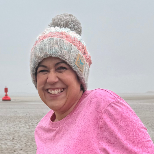 A freezing cold Claire, the owner of Waves and Wild Water, is trying to embrace the moment on the beach in the rain in South Wales. But it's ok, at least she is wearing her knitted beanie hat in Seashell Pink!