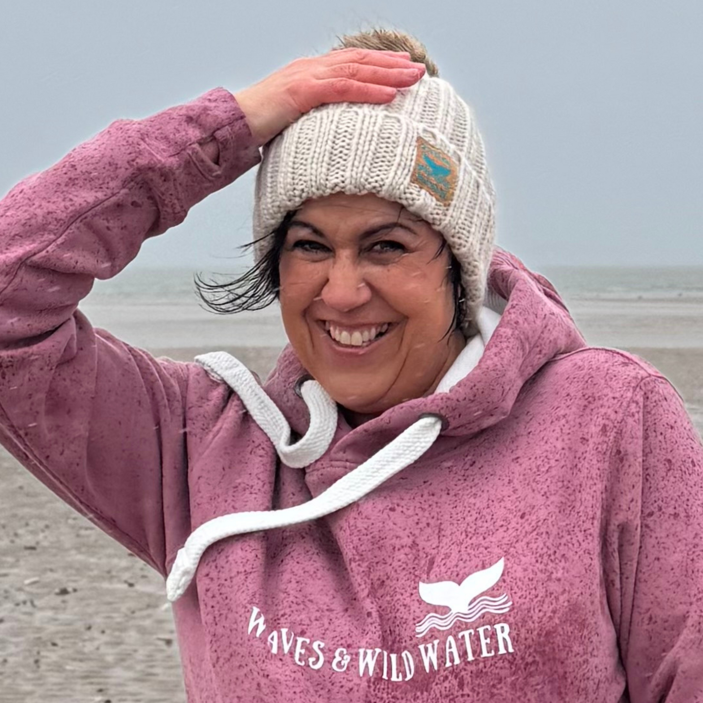 It's a bit wet and windy on the beach in South Wales, but wild swimmer and sea dipper Claire, is wearing her Winter Swim knitted beanie hat and her Sunset Blush hoodie.