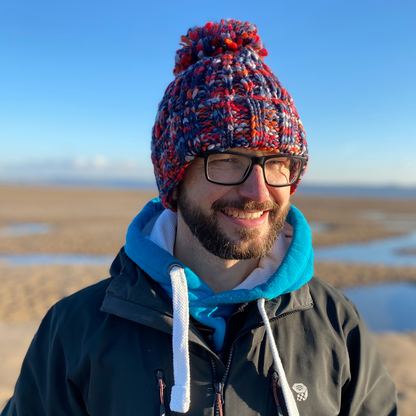 This is our gorgeous chunky knitted beanie hat in Campfire Embers colours. It's called Campfire Embers because the chunky knit is in various shades of red, orange and blue - just like a beach campfire! It has a deep fold up cuff to keep your ears snug and cosy and is finished off with a plump woolly pom pom. Glenn is wearing her hat on the beach after an invigorating swim in the sea.