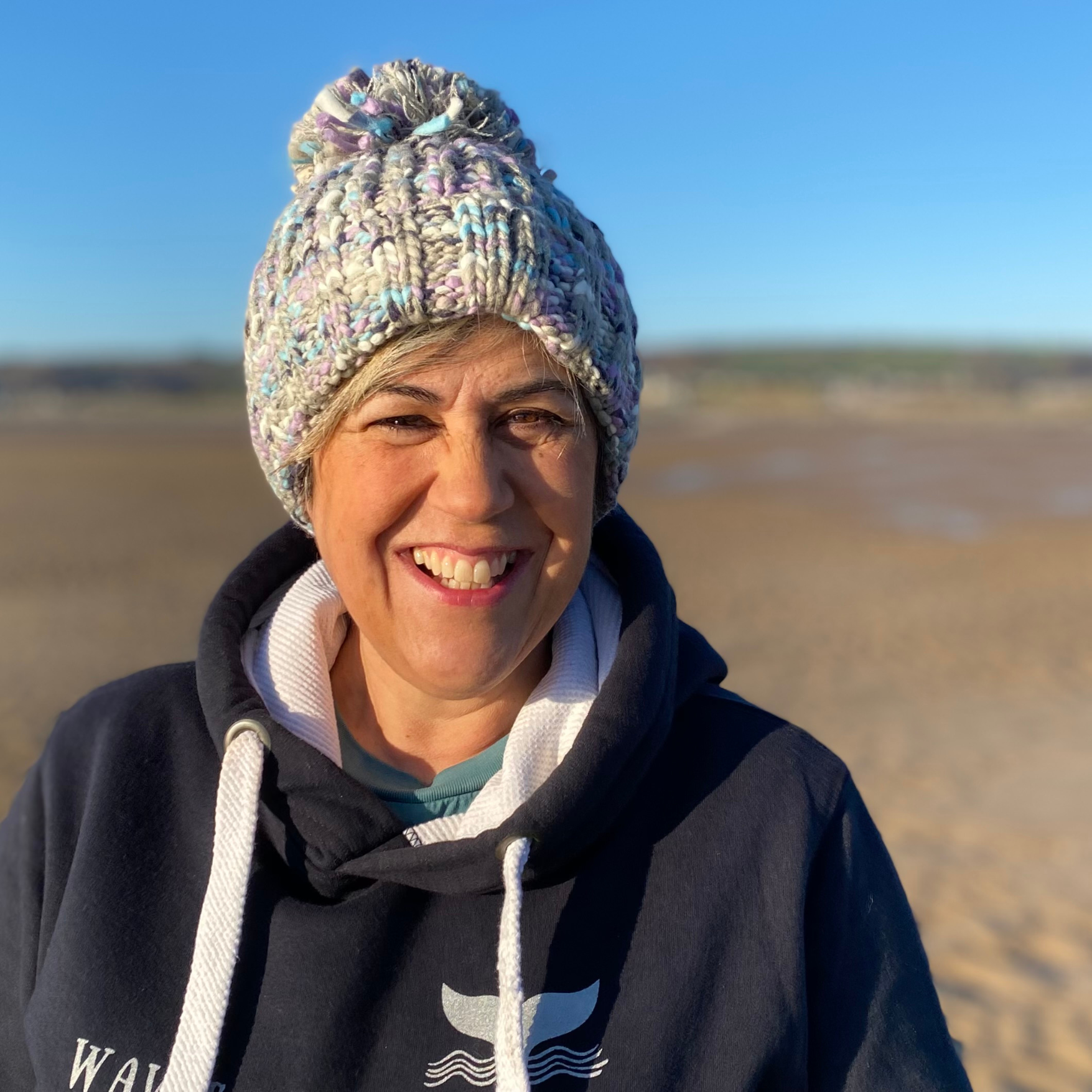 Wild swimmer Claire, wears her Waves and Wild Water chunky pom pom beanie on the beach in Wales. The gorgeous greys and lilacs make this hat a perfect compliment to her Midnight Waves hoodie.