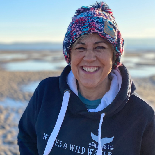 Wild swimmer and cold water therapist Claire, enjoys some winter sun on the beach, whilst staying cosy in her chunky knitted beanie hat. Knitted in beautiful shades of blue and pink, and finished off with a chunky statement pom pom.