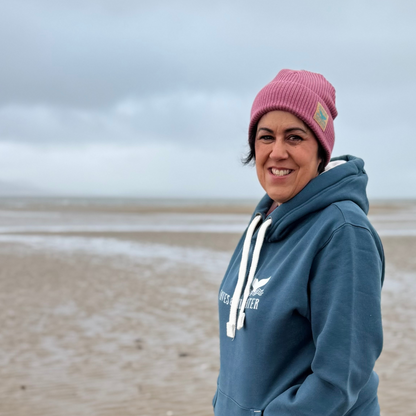 Waves and Wild Water owner and sea dipper Claire, pairs her Sunset Blush Fisherman Beanie with a Stormy Sea hoodie to keep her warm and cosy on a beach walk in Wales.