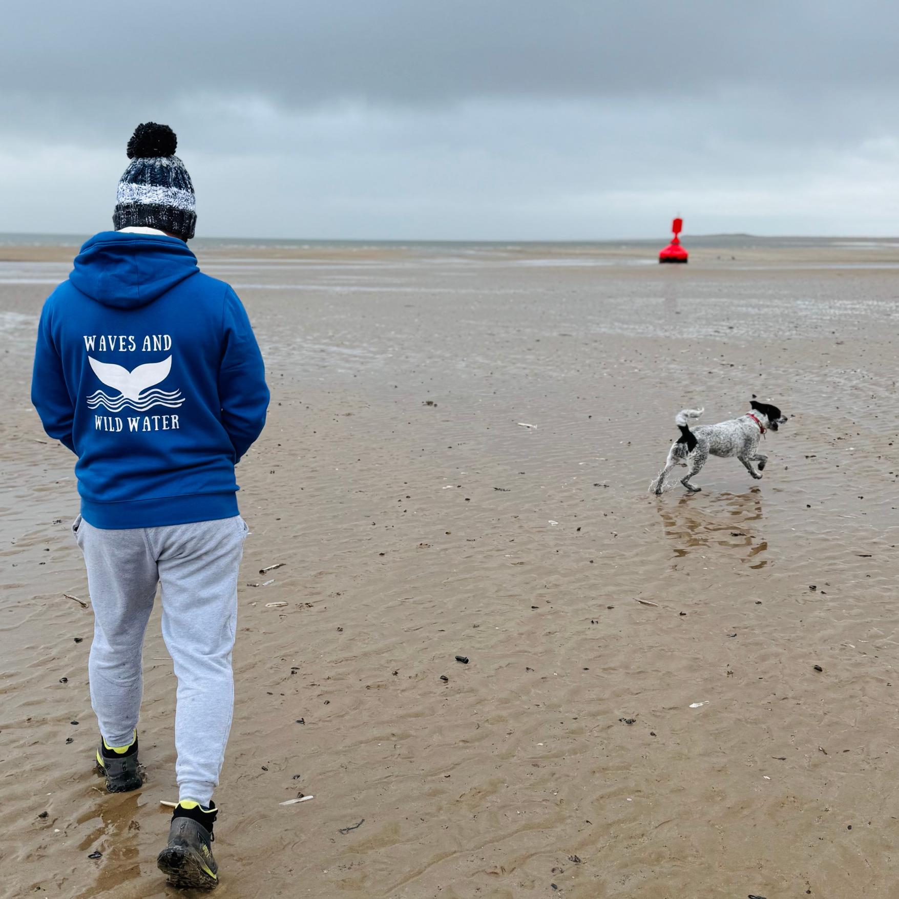 Waves and Wild Water owner and wild swimmer Glenn, wears his Swimmer Blue hoodie while working the dog on the beach in South Wales. It's pretty cold but he's cosy in his hoodie and hat.