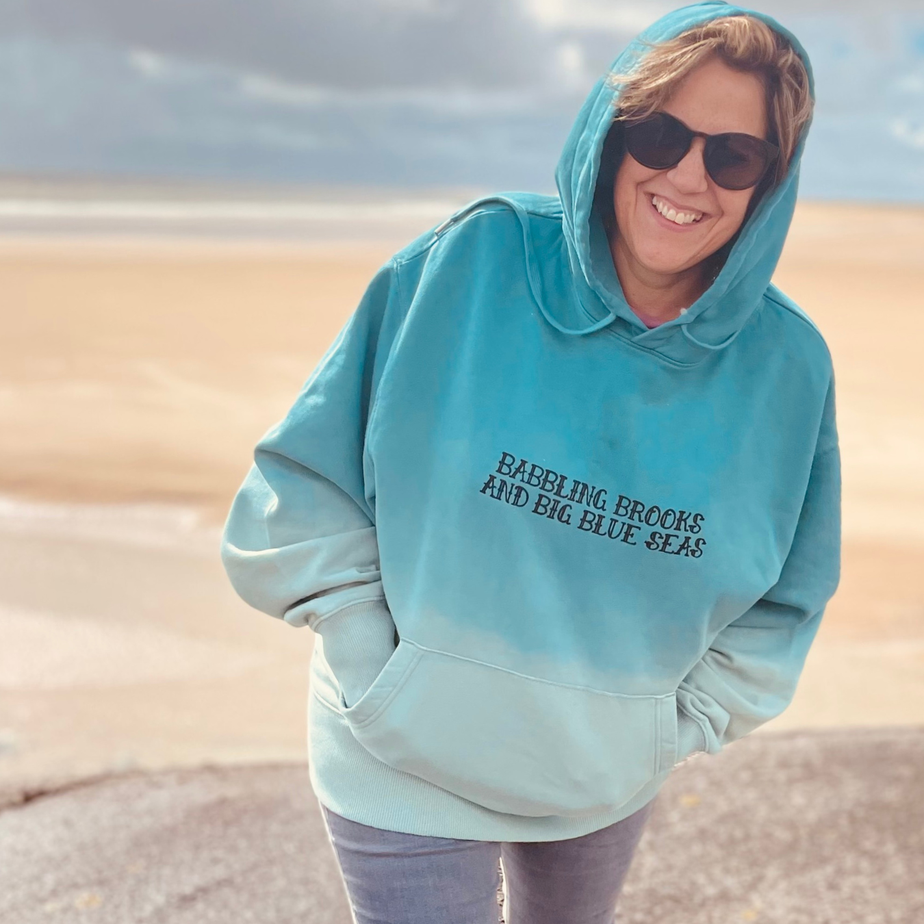 Waves and Wild Water owner, Claire, shows off her Babbling Brooks hoodie against the perfect backdrop of a South Wales beach.