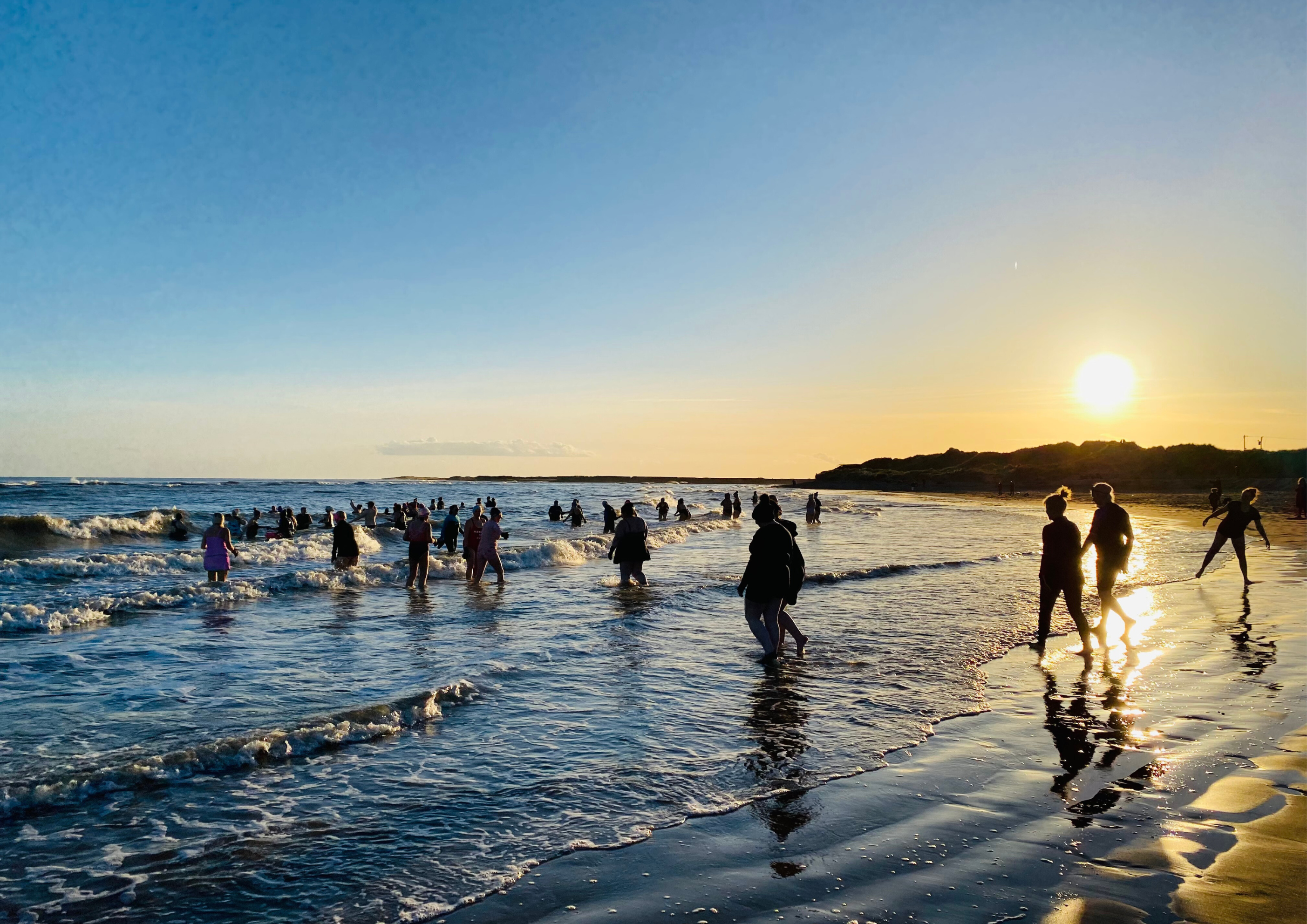 Wild swimmers, sea dippers, and cold water adventurers enjoy the waves as the sun goes down over the sea in South Wales.