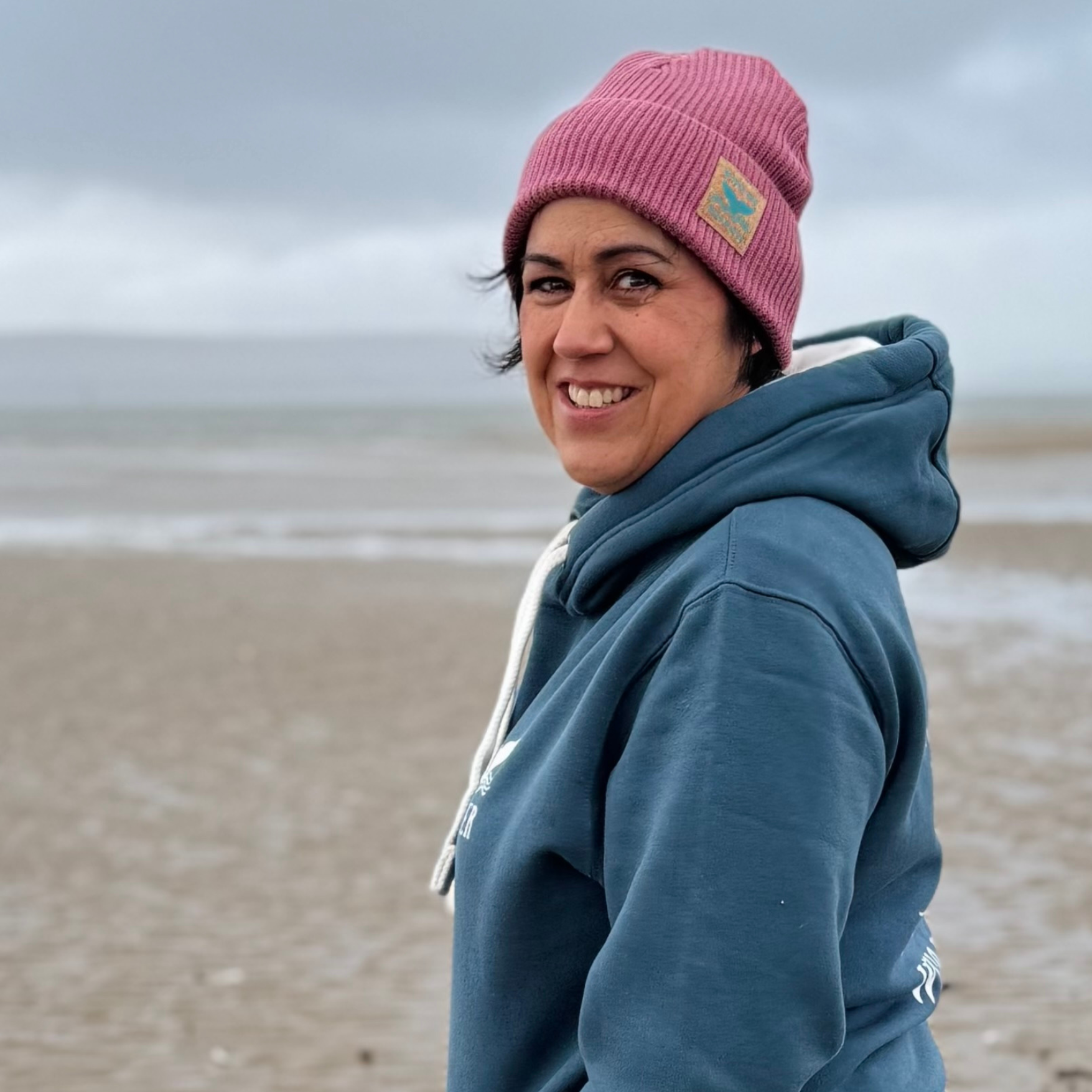 Waves and Wild Water owner and wild swimmer Claire, wears her gorgeous Stormy Sea hoodie to stay warm and cosy during her walk on the beach in Wales.