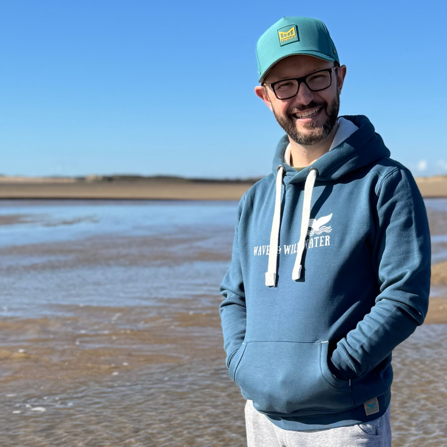 Outdoor swimmer Glenn, takes a break from cold water dipping to enjoy a sunny walk on the beach. Although he's wearing his Waves and Wild Water hoodie in Storm Sea, there's not a wave to be seen.