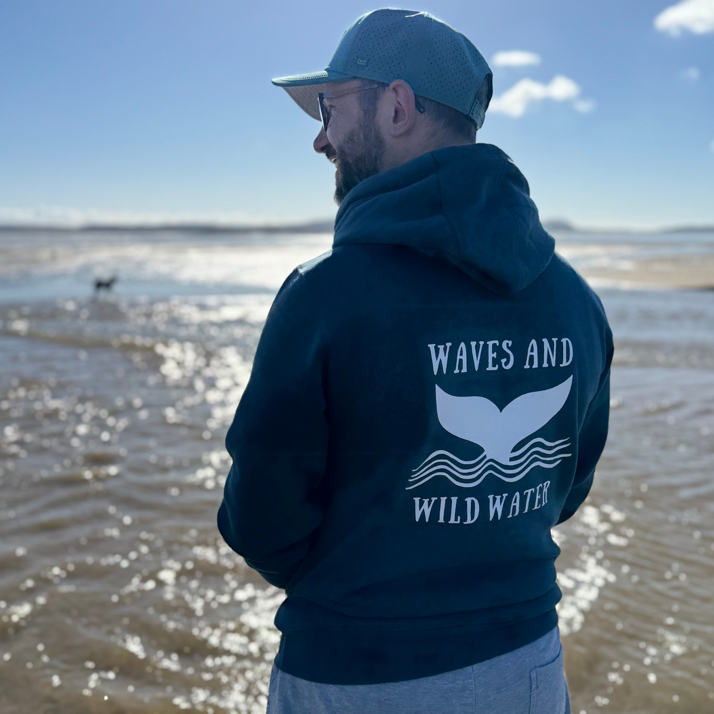 Waves and Wild Water owner Glenn, looks happy to be snug and warm in his Stormy Sea hoodie as he enjoys a bright, early spring walk on the beach. The white whale tail logo across his back looks fab in the sun, and perfectly compliments the bluey green colour of the hoodie.