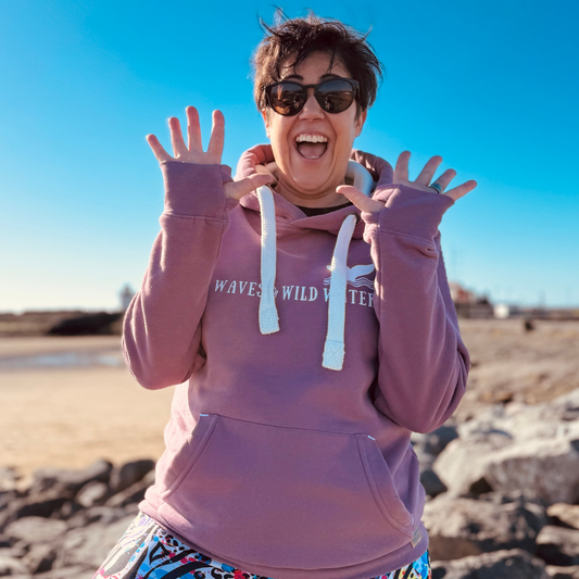 Waves and Wild Water owner and wild swimmer Claire, delightfully shows off her hoodie cuff thumb holes! She's wearing her gorgeous hoodie in beautiful Sunset Blush pink.