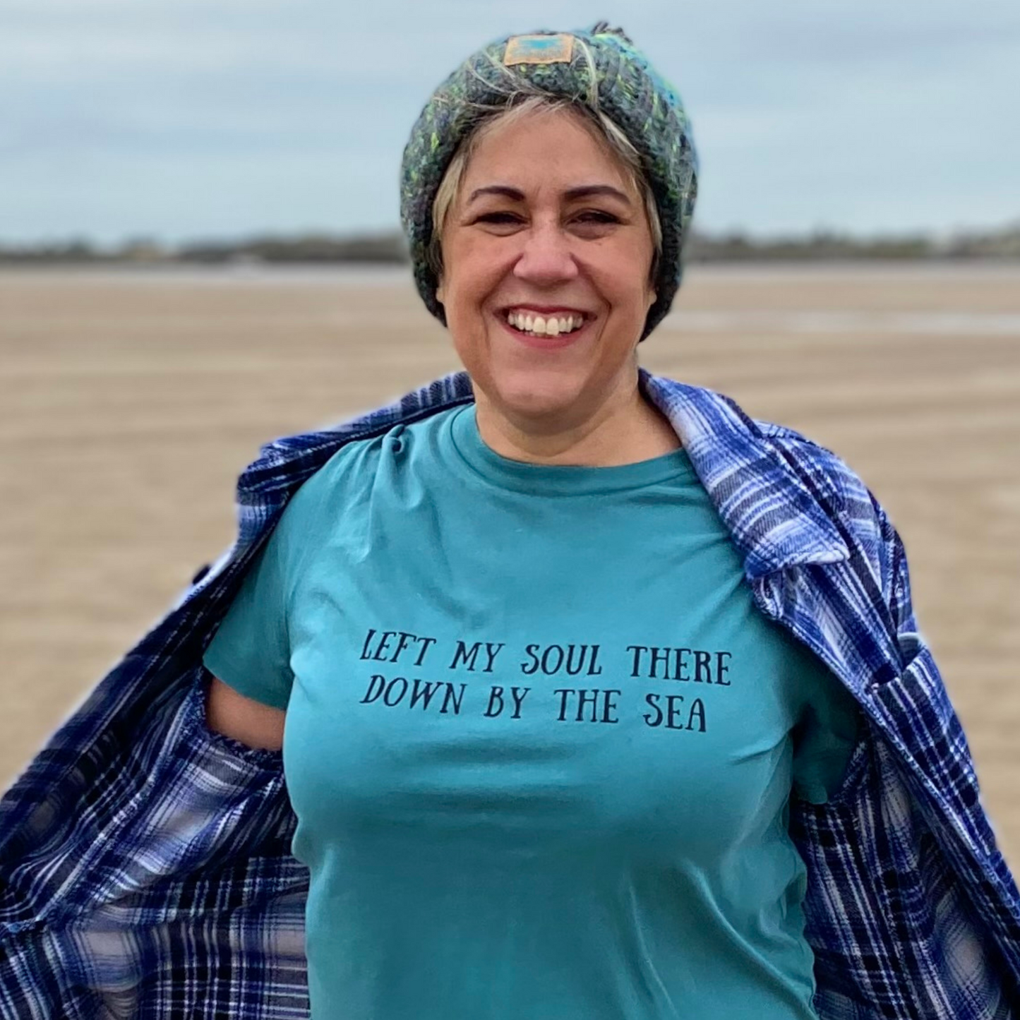 Waves and Wild Water owner Claire, styles her vintage green 'Down by the Sea' t-shirt with a knitted beanie and checked shirt. Low tide at the beach provides the perfect background and emphasises that Claire's soul is truly found at the sea.