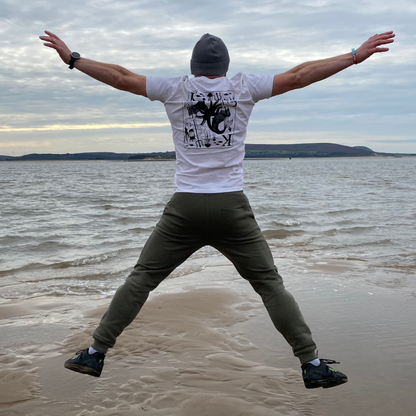 Glenn jumps for joy at the sight of the sea and celebrates the splendour of his white King Of Seas t-shirt with the playing card style design on the back.
