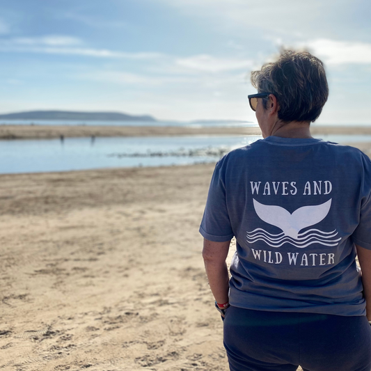 Claire from Waves and Wild Water wears her grey wild swimming inspired organic cotton t-shirt whilst looking out towards the Gower in South Wales. The large white hand printed logo on the back of her tee looks great in the sun.