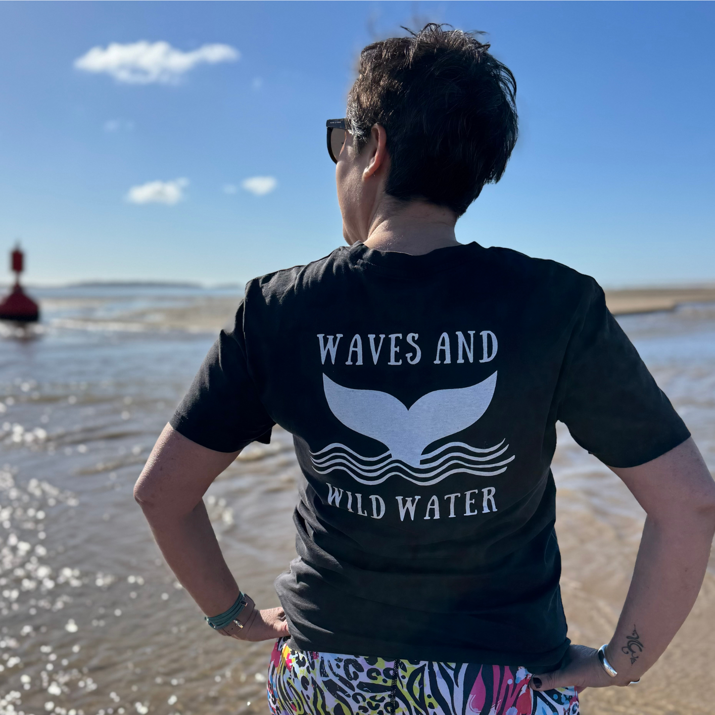 Taking a moment to enjoy the sun on the beach in Wales, Waves and Wild Water owner Claire, wears her Night Sky tee with pride. The bright white printed whale tail logo looks great against the black backdrop of the t-shirt.