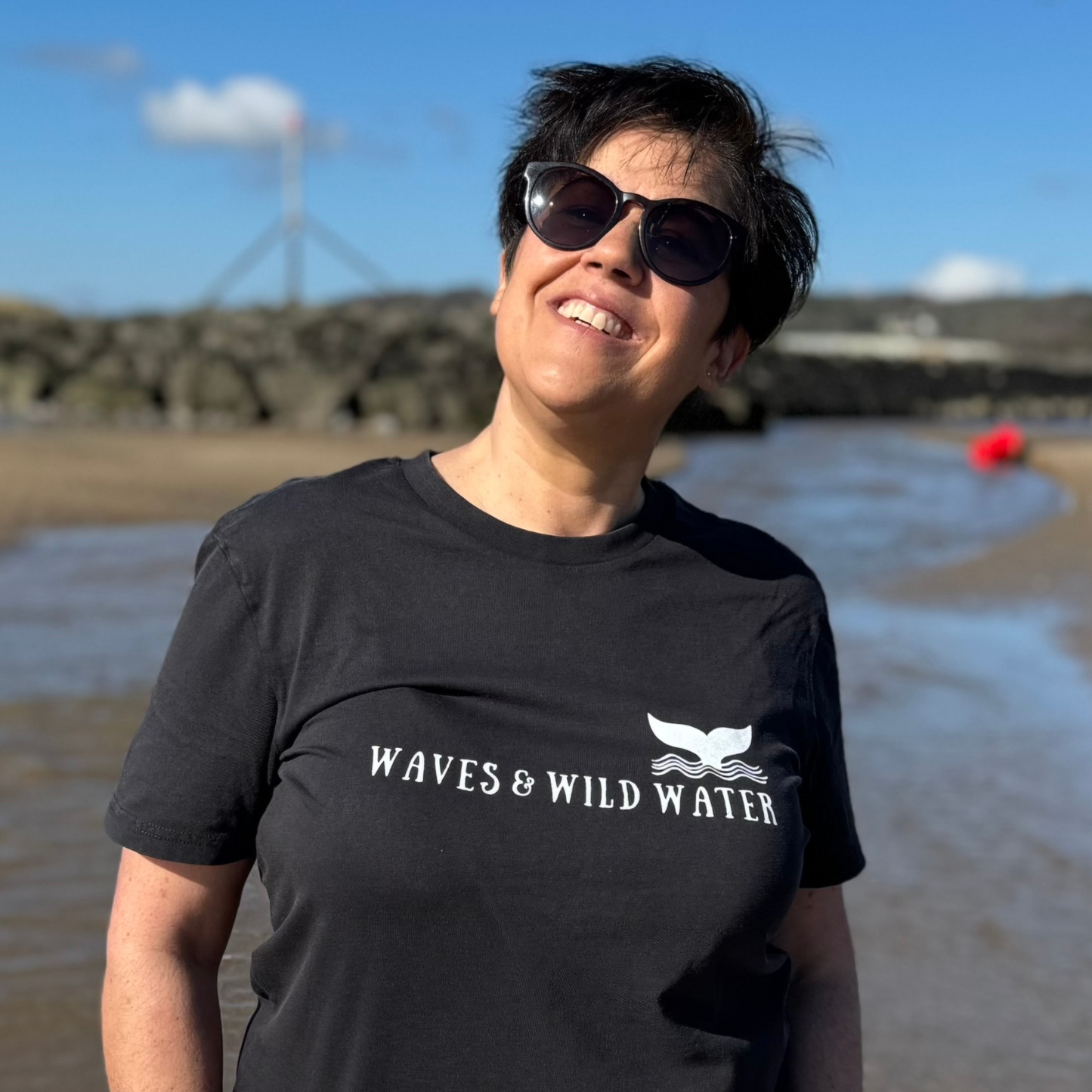 What is that glowing yellow thing in the sky? Is it the sun?? Wild swimmer Claire enjoys a sunny walk on the beach while wearing her black Waves and Wild Water t-shirt with white printed logo.