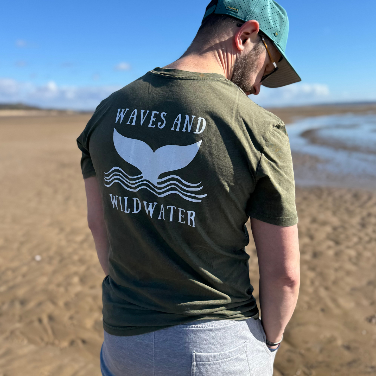 Outdoor swimmer Glenn, wears his Waves and Wild Water t-shirt in River Bed green, while enjoying a sunny walk on the beach in South Wales.