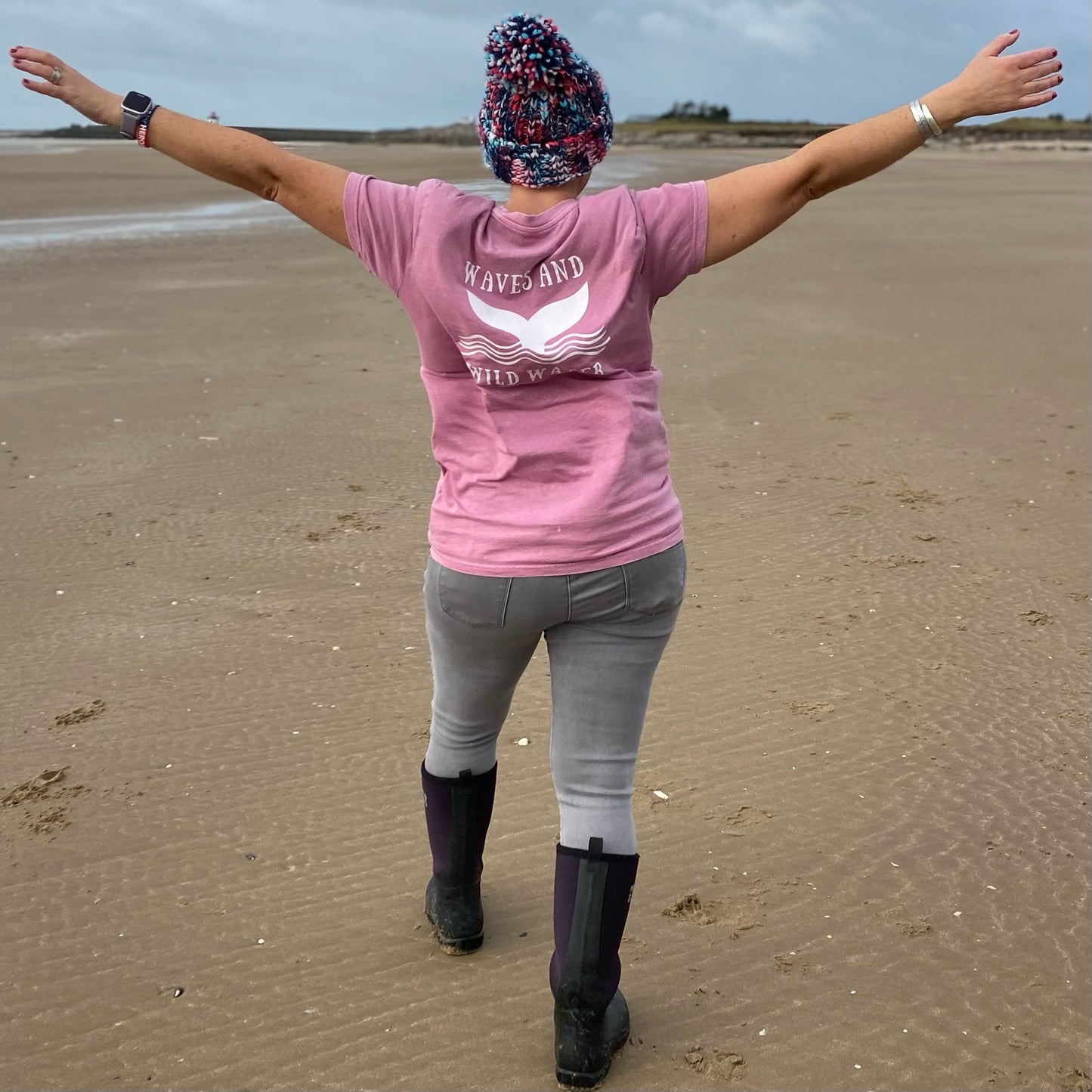 Waves and Wild Water Claire, braves the windy beach in her gorgeous Seashell Pink t-shirt with the striking whale tail logo on the back in white.