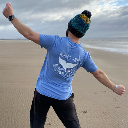 Proudly showing off his love for wild swimming and sea dipping adventures, Waves and Wild Water owner Glenn, braves the elements on the beach in his vintage style Swimmer blue t-shirt, with fabulous whale tail logo in white on the back.
