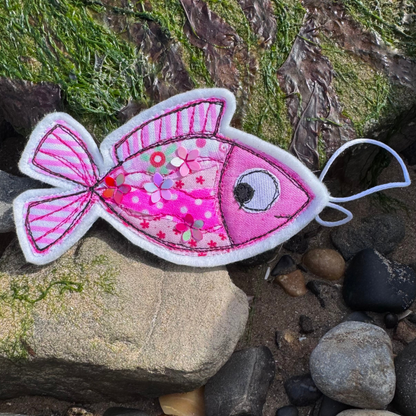 Fish Wish hanging decoration in pink tones, resting on seaweed-covered rocks, a small handmade keepsake filled with coastal charm. Only from Waves & Wild Water.