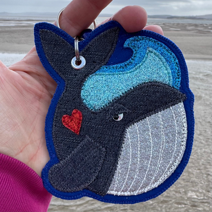 Wyn the Whale keyring resting in hand by the shoreline, a gentle ocean companion carrying a little piece of the sea wherever he goes. Created by the sea in Wales for wild swimmers and sea life lovers.