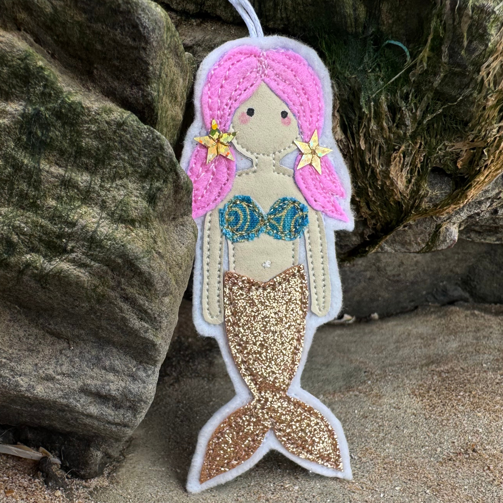 Handmade Wild Water Mermaid, from Waves & Wild Water. Golden glitter tail with patterned bikini top displayed on coastal rocks. Perfect gift for wild water swimmers.