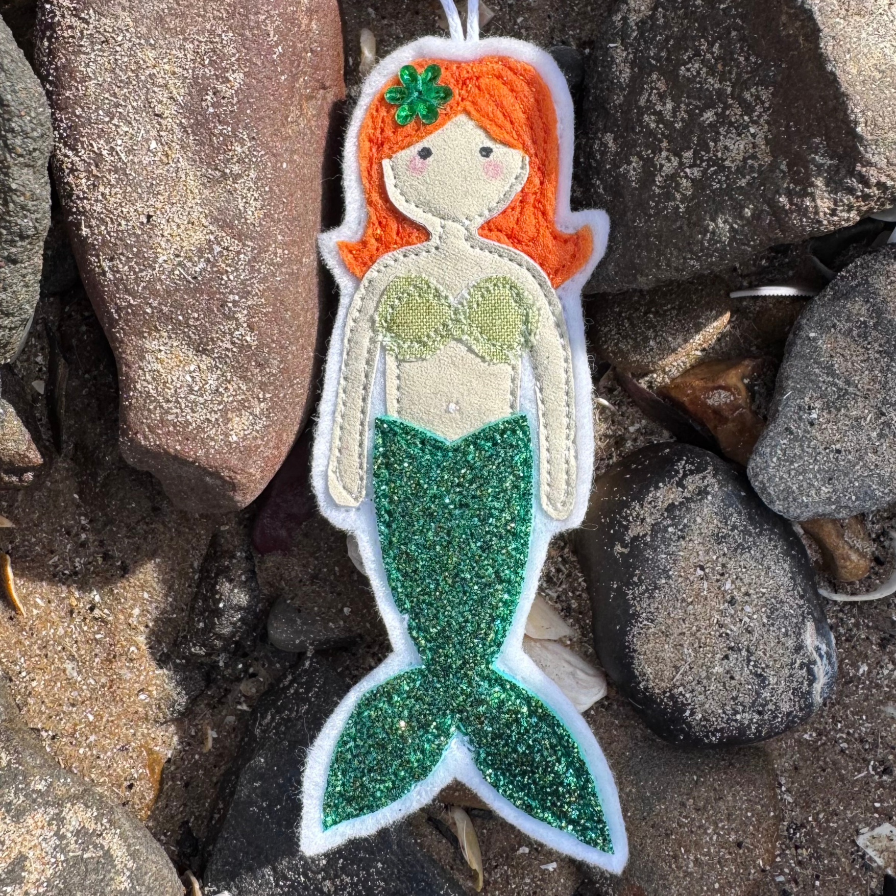 Wild Water Mermaid decoration with shimmering green tail resting among seaside stones, a unique handmade coastal gift - only from Waves & Wild Water.