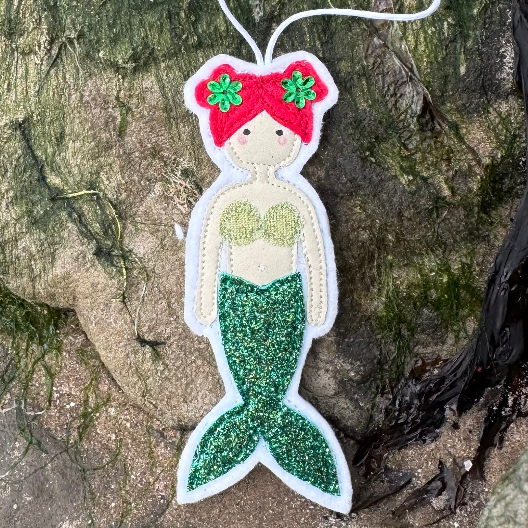 Handmade green glitter tail mermaid hanger with coordinating bikini top displayed on coastal rocks. Only from Waves & Wild Water - a perfect gift for the wild wannabe mermaid in your life.