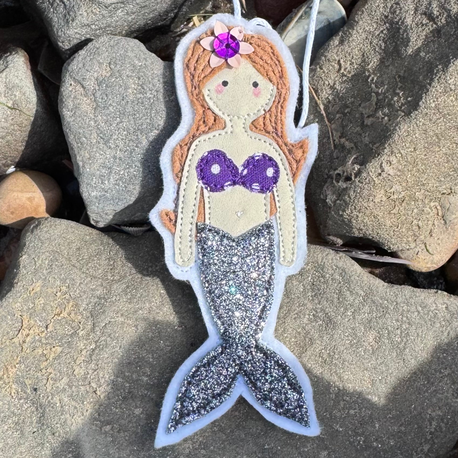 Wild Water Mermaid decoration with shimmering silver tail resting on smooth seaside stones, a unique handmade coastal gift - only from Waves & Wild Water.