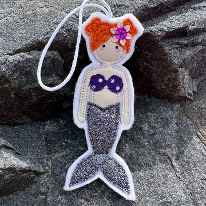 Handmade grey glitter tail mermaid hanger with purple polka dot bikini top displayed on coastal rocks.
