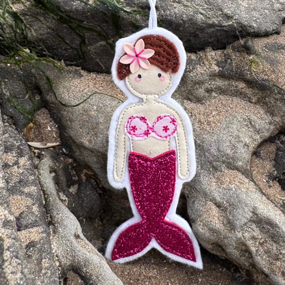 Handmade pink glitter tail mermaid hanger with patterned bikini top displayed on coastal rocks. Lovingly made by Waves & Wild Water on the Welsh coast.