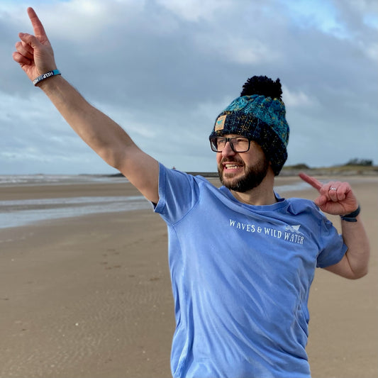 Man on a beach wearing a blue t-shirt and pom pom hat.