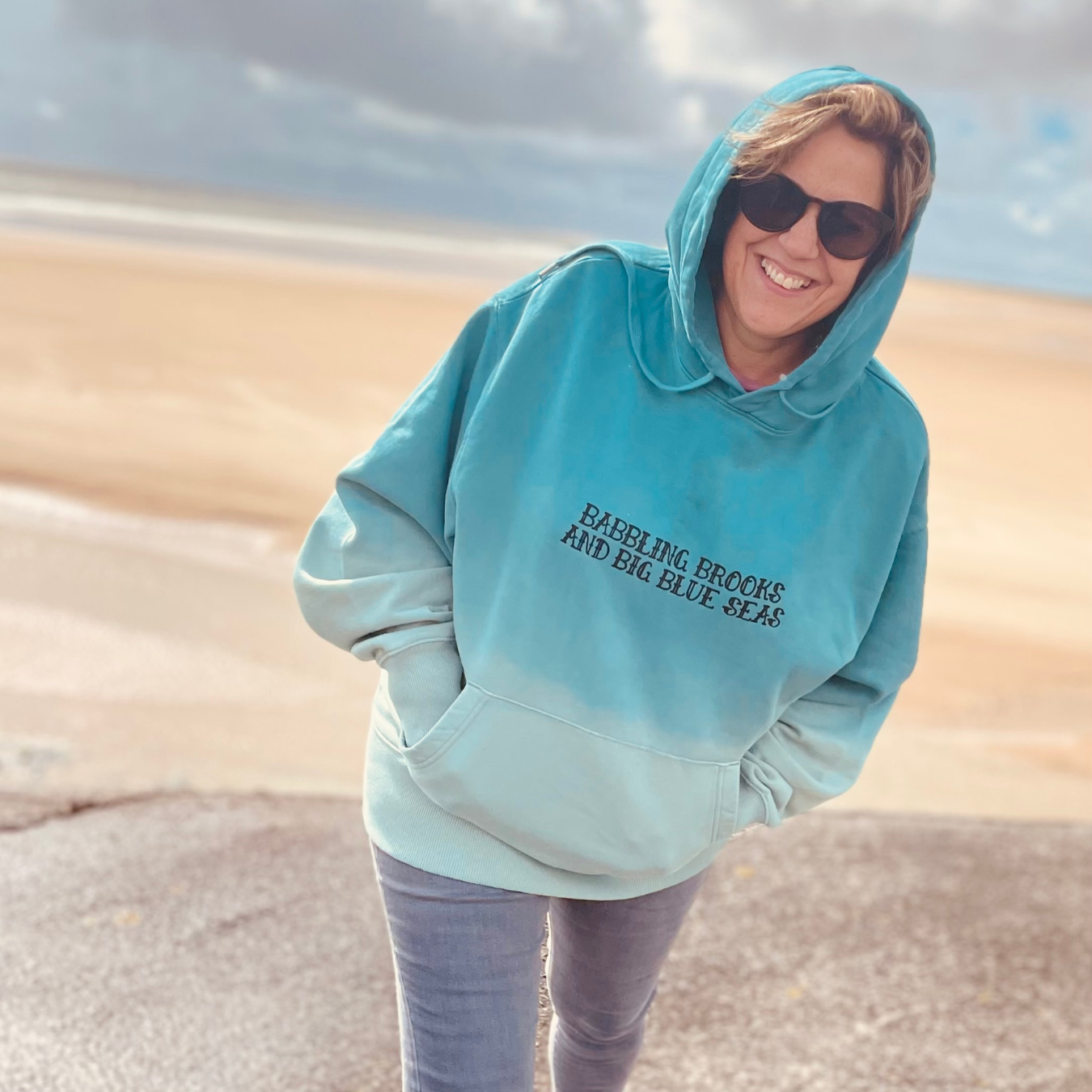 A woman wearing a blue hoodie with the words 'Babbling Brooks And Big Blue Seas' printed across the front.