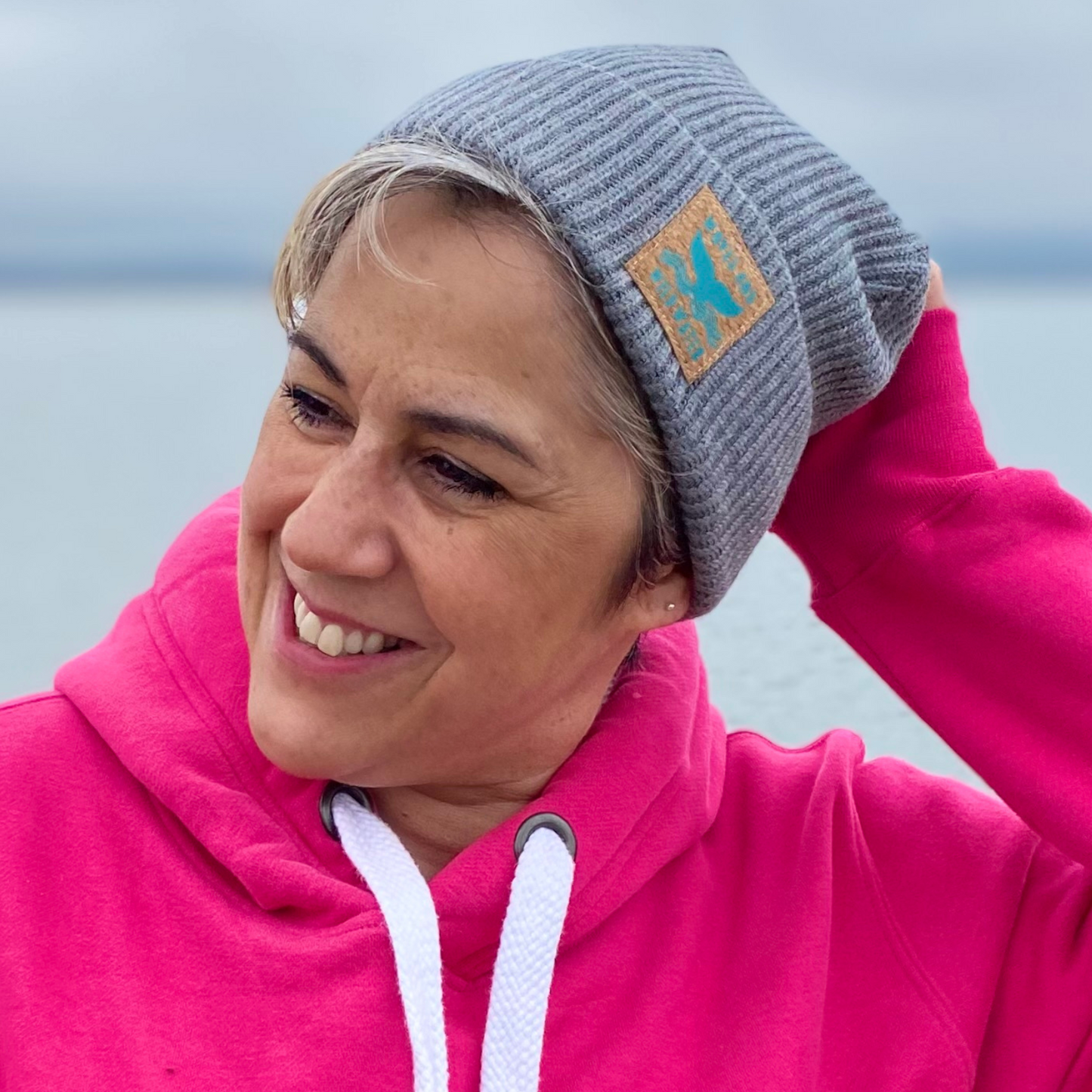 A woman in a pink hoodie and wearing a grey fisherman beanie hat.