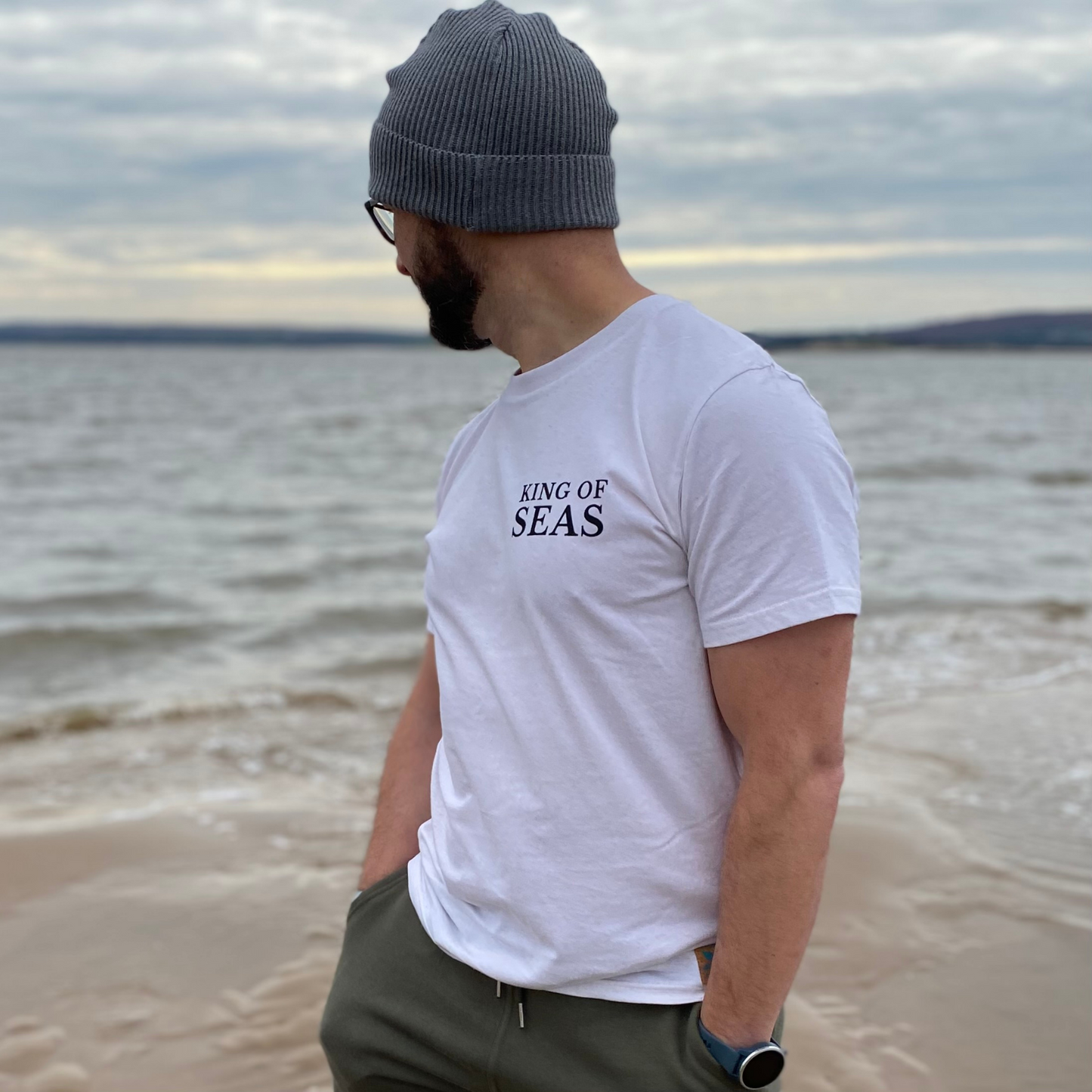 A man wearing a t-shirt with 'King Of Seas' printed on it and a grey beanie hat.