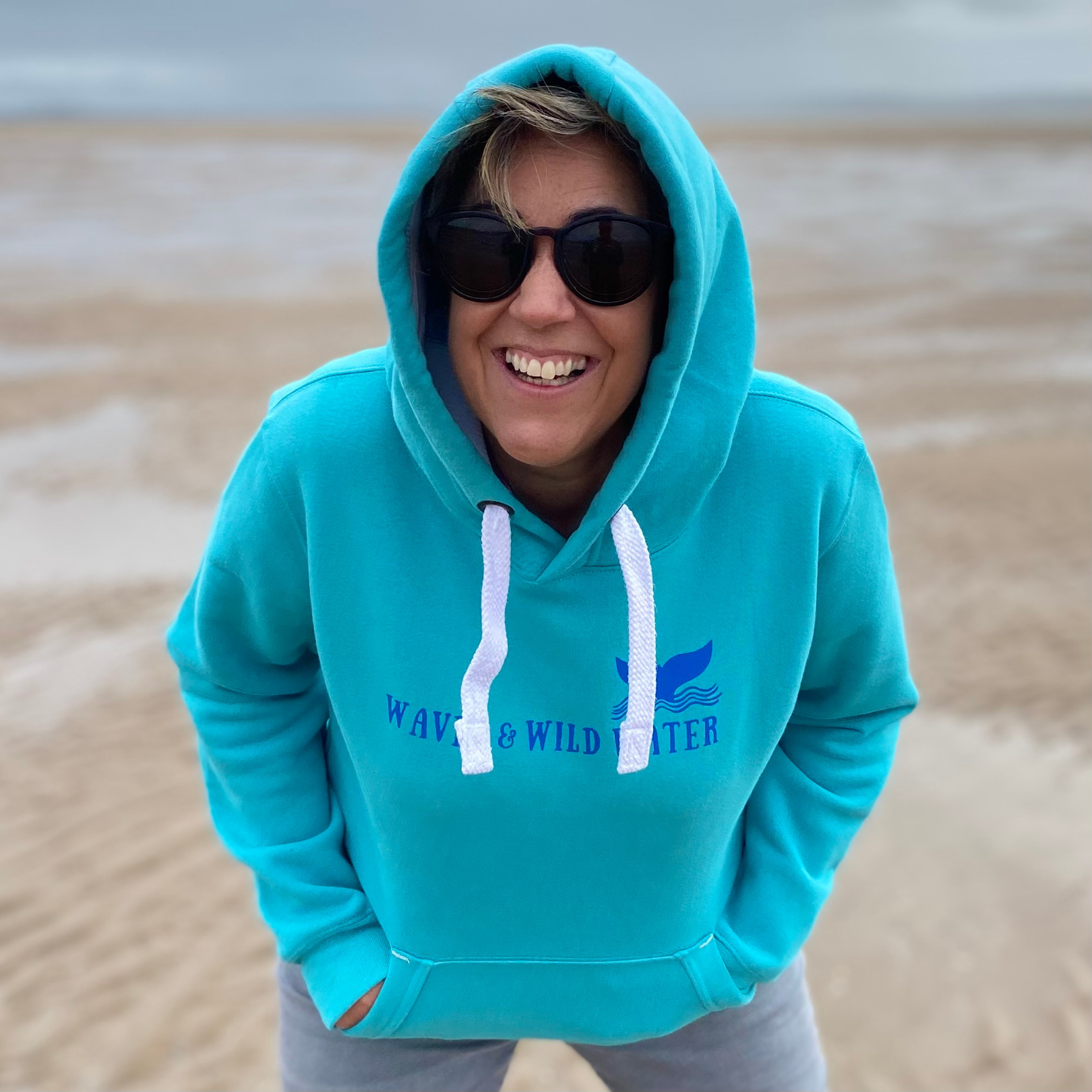 A woman wearing a lagoon blue hoodie with the hood up.
